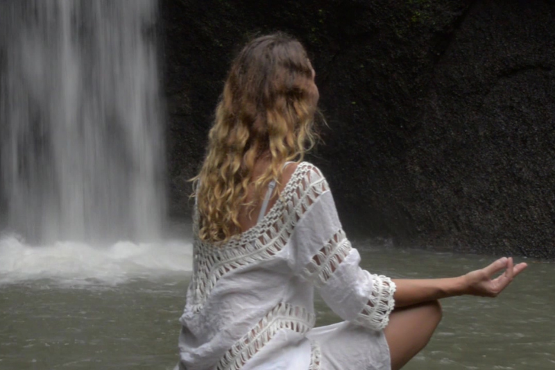 Femme assise méditant devant une cascade